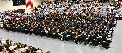 wide shot of graduates sitting at commencement and audience in the background