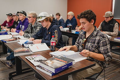 group of students sitting in classroom reviewing textbook