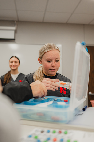 Students practicing a medical injection technique using a training kit in a classroom setting.