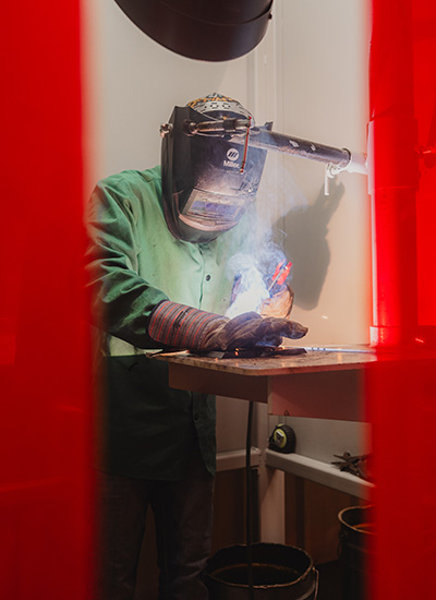 student wearing welding gear welding in booth