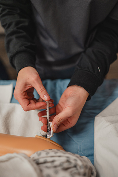 Student practicing an injection on a training mannequin.