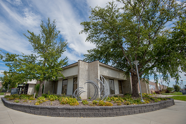 Modern building with trees, garden beds, and outdoor sculpture.