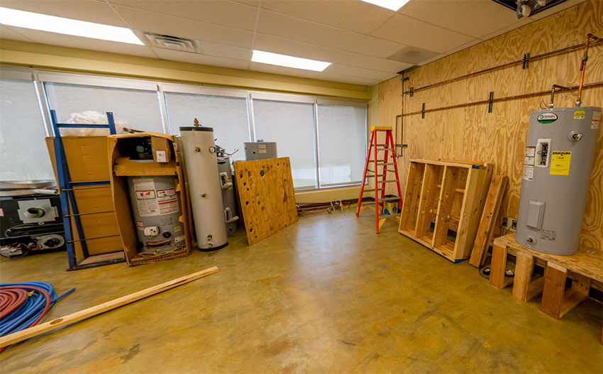 Plumbing lab with water heaters, framing mockups, piping materials, and workstations used for hands-on plumbing training.