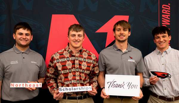 4 students in front of Northeast backdrop holding signs saying Northeast, Scholarships, Thank you, and Hawk logo
