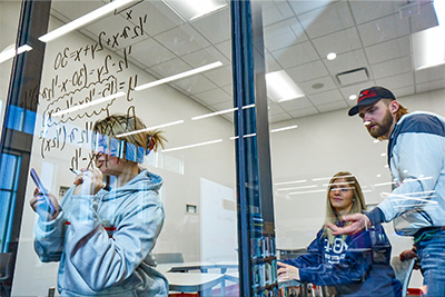 Students working on math equation written on glass wall