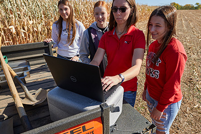Students and instructor on laptop in cornfield