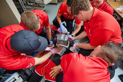 EMT students practice cardiac arrest response using a LUCAS mechanical CPR device and bag-valve-mask ventilation in a training lab.