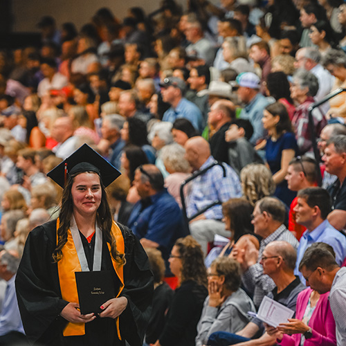 graduate walking with diploma in front of crowd