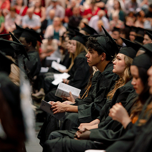 graduates seated for ceremony with audience in background